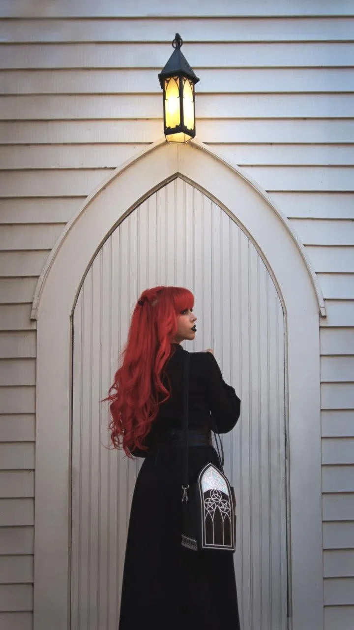 Women with long red hair and a long black dress with a gothic-styled bag hanging from her shoulder.