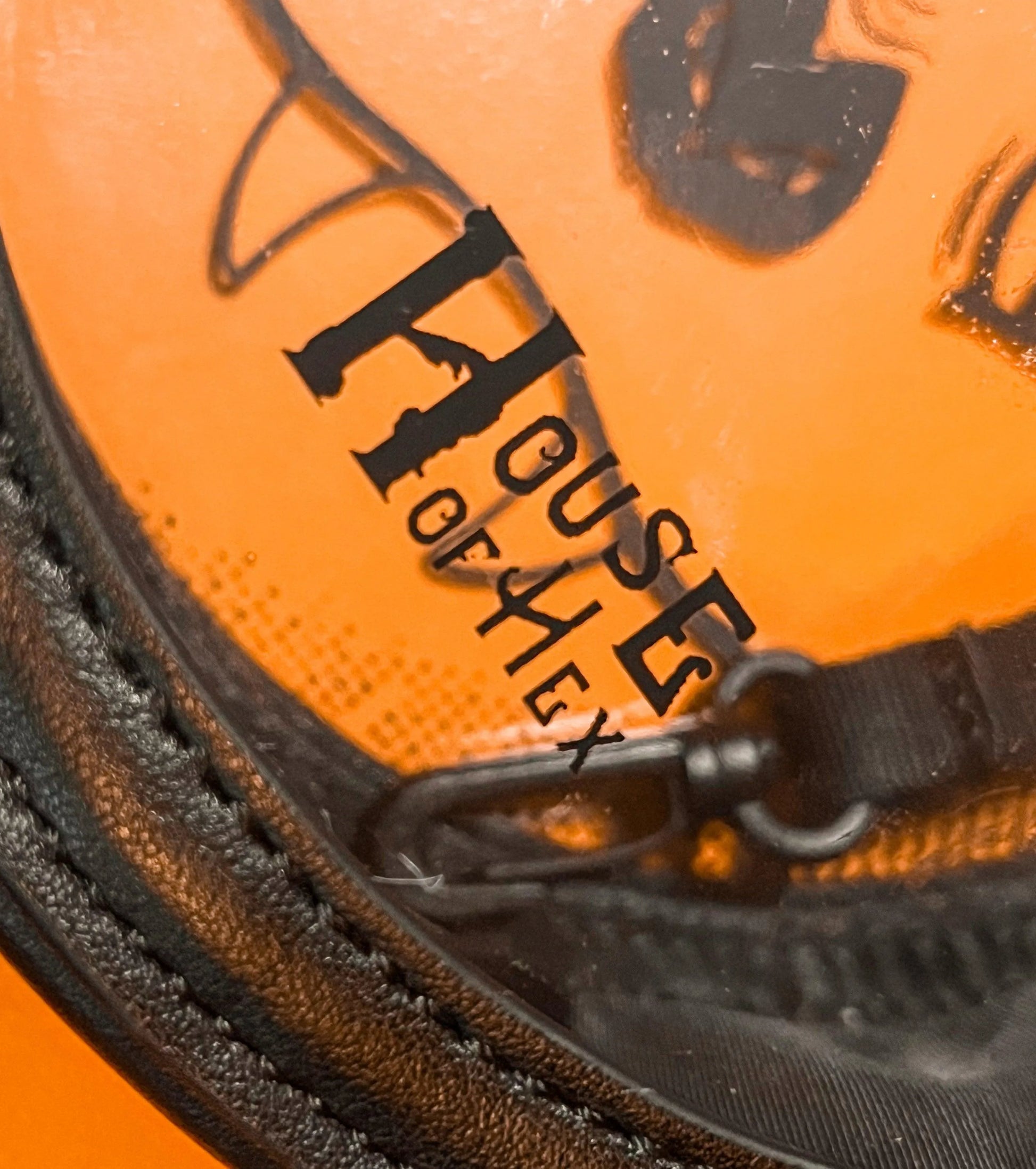 Close up of a black bag on an orange background showcasing the words "House of Hex" in a gothic font.