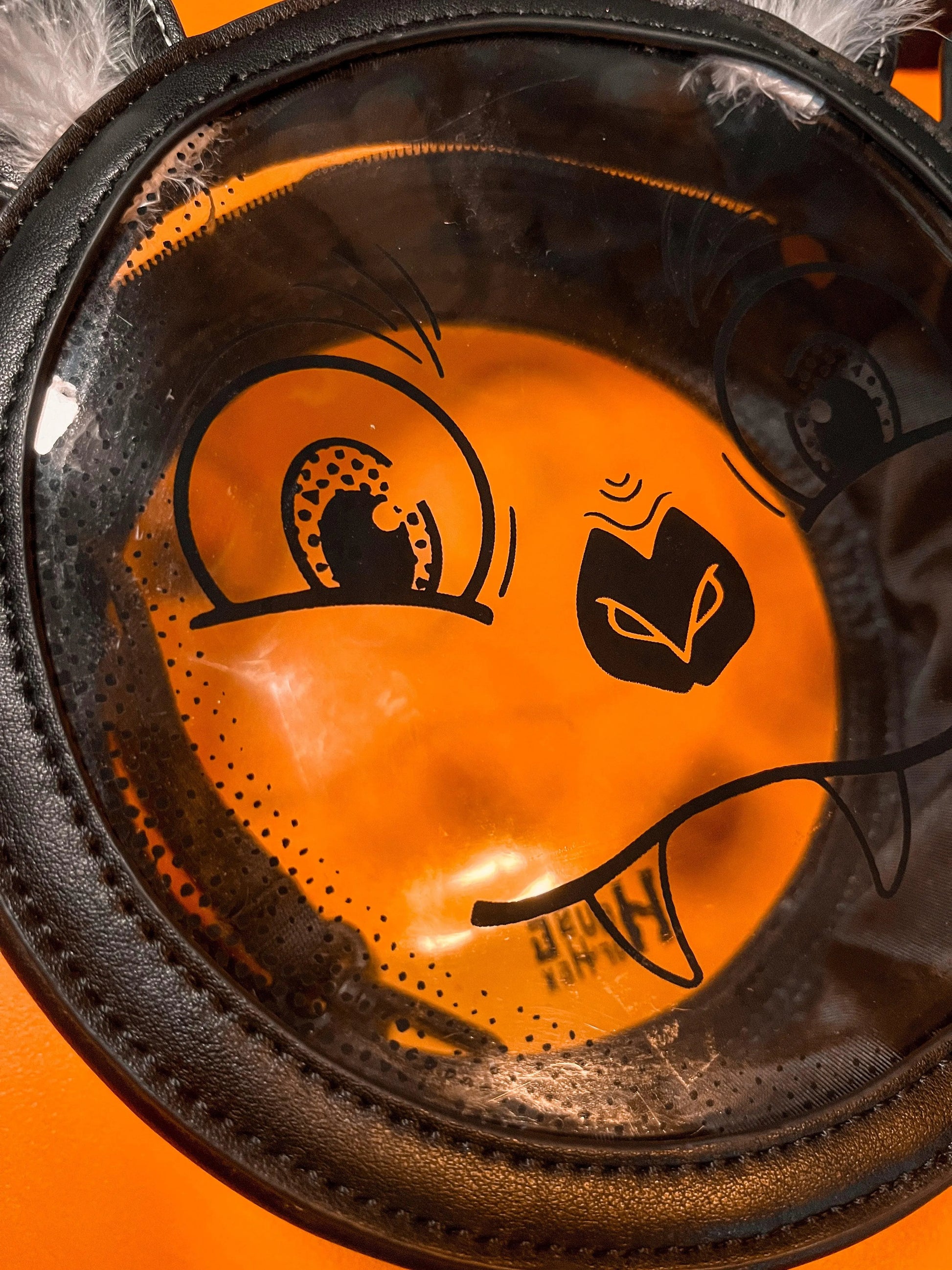 A Halloween purse featuring a whimsical bat face design that's clear in the center sitting on an orange background.