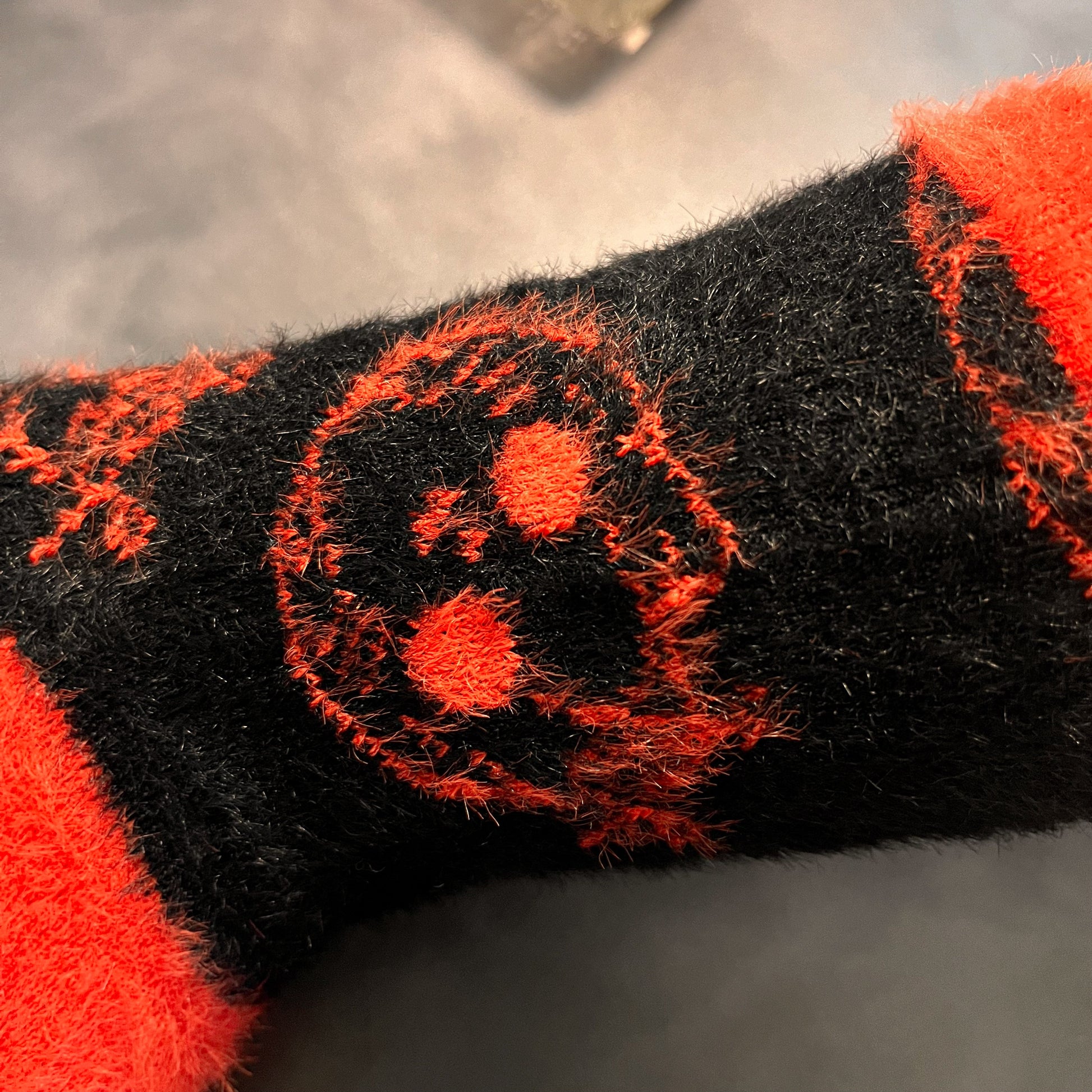 Black fuzzy socks with orange on the toe, heel, and ankle featuring a pattern of pumpkin shaped cat heads.