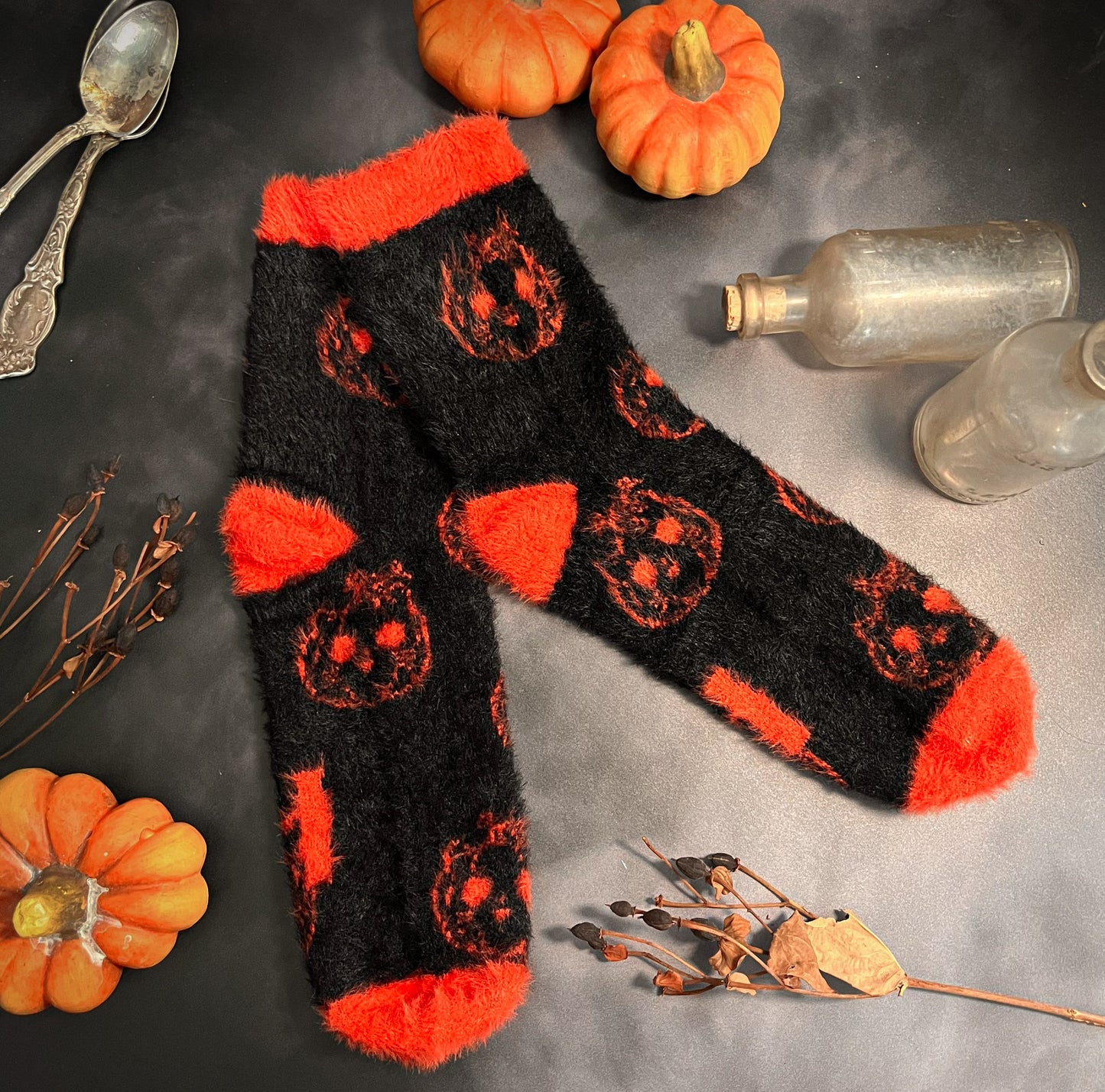 Black fuzzy socks with orange on the toe, heel, and ankle featuring a pattern of pumpkin shaped cat heads.