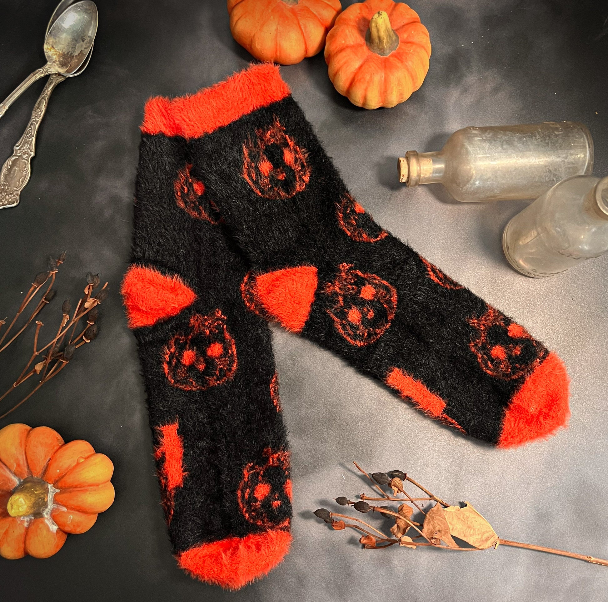 Black fuzzy socks with orange on the toe, heel, and ankle featuring a pattern of pumpkin shaped cat heads.