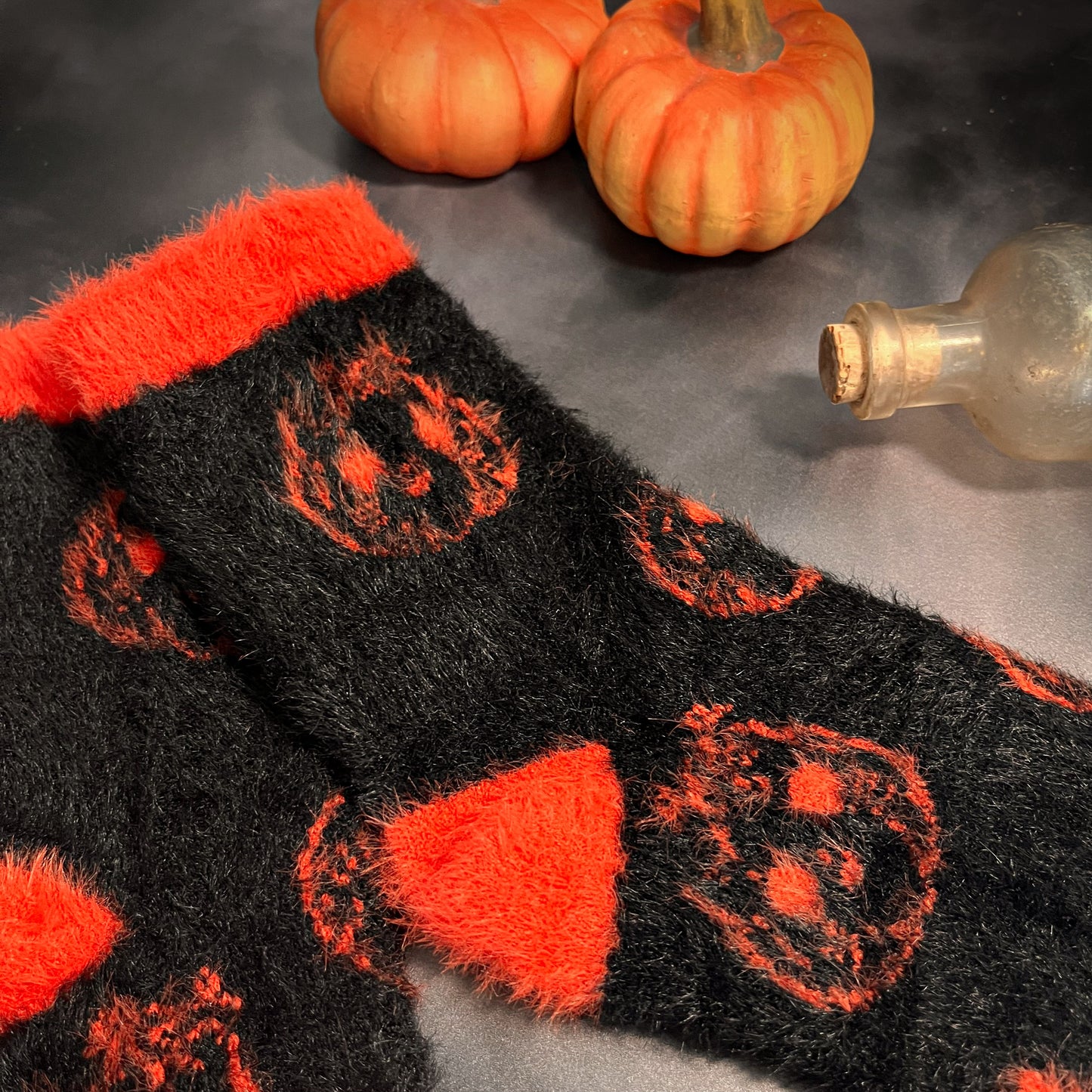 Black fuzzy socks with orange on the toe, heel, and ankle featuring a pattern of pumpkin shaped cat heads.