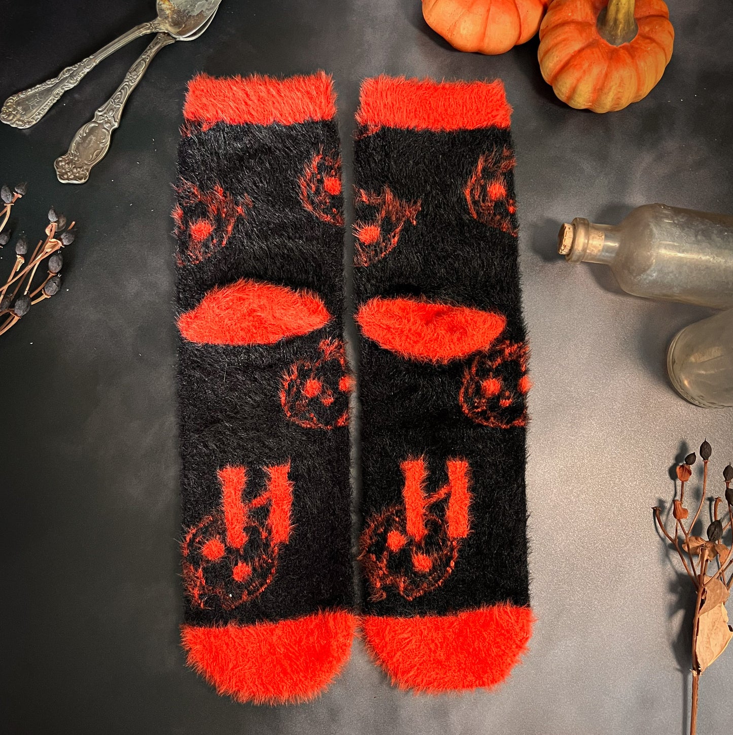 Black fuzzy socks with orange on the toe, heel, and ankle featuring a pattern of pumpkin shaped cat heads.