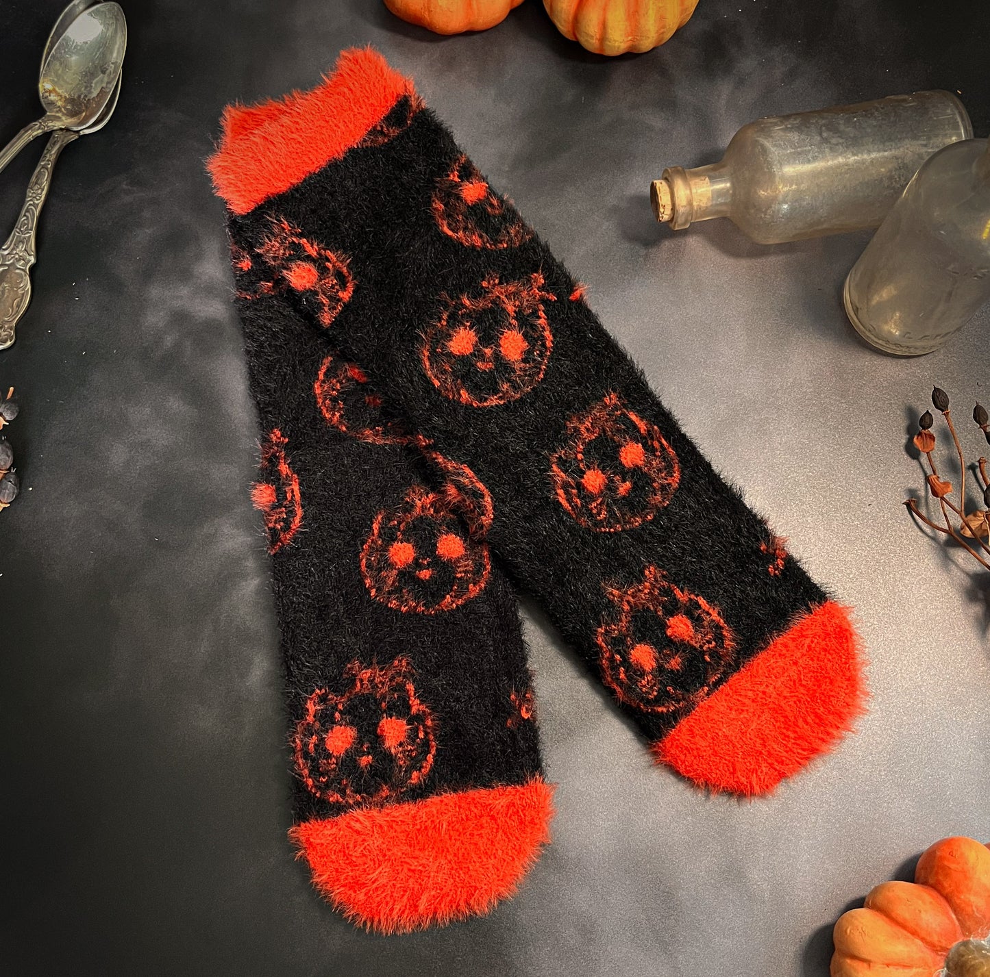 Black fuzzy socks with orange on the toe, heel, and ankle featuring a pattern of pumpkin shaped cat heads.