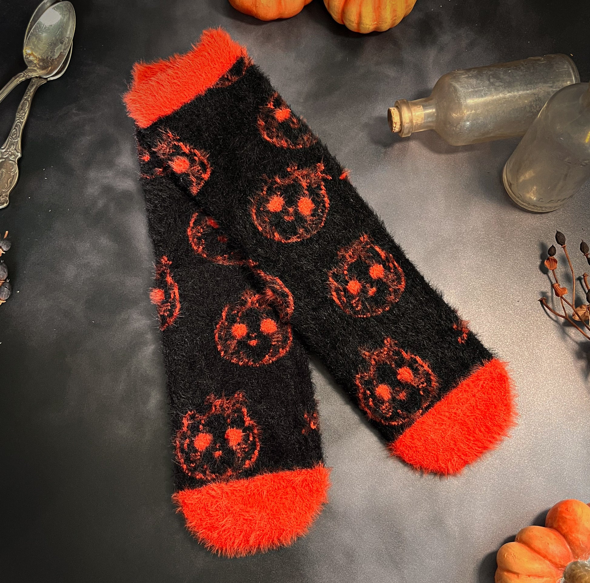 Black fuzzy socks with orange on the toe, heel, and ankle featuring a pattern of pumpkin shaped cat heads.