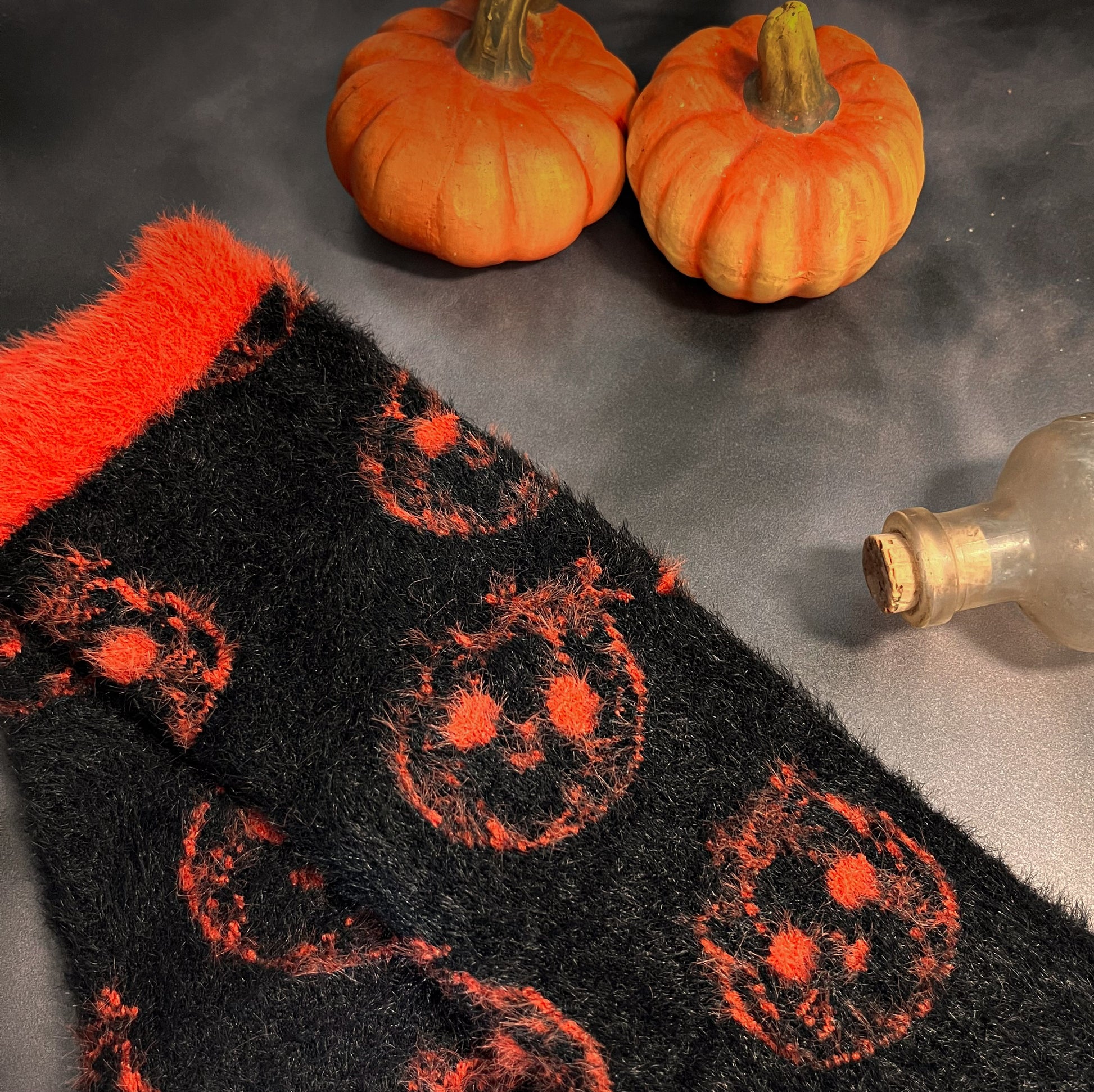 Black fuzzy socks with orange on the toe, heel, and ankle featuring a pattern of pumpkin shaped cat heads.