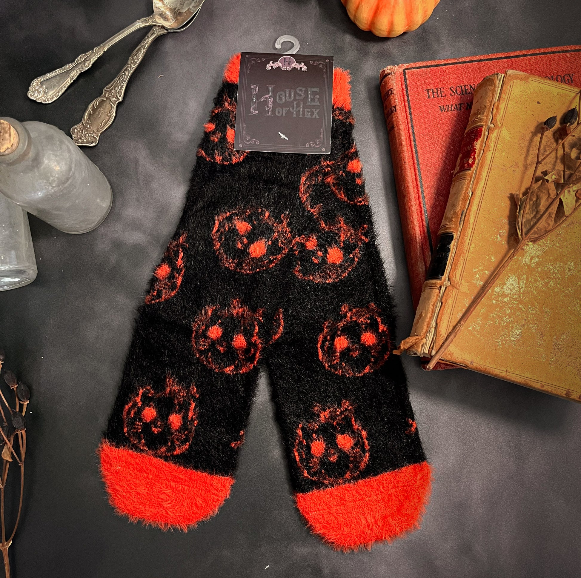 Black fuzzy socks with orange on the toe, heel, and ankle featuring a pattern of pumpkin shaped cat heads.