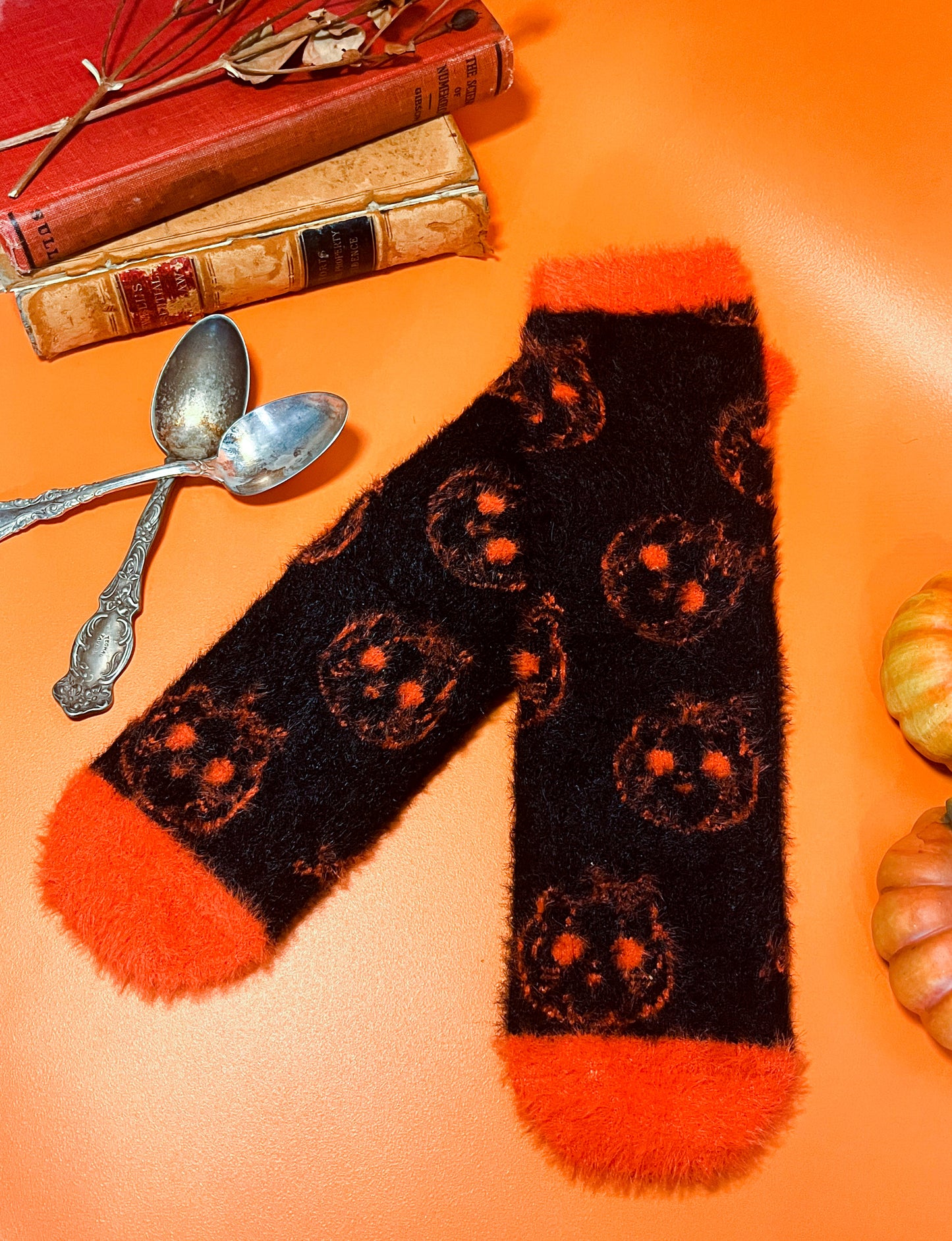 Black fuzzy socks with orange on the toe, heel, and ankle featuring a pattern of pumpkin shaped cat heads.