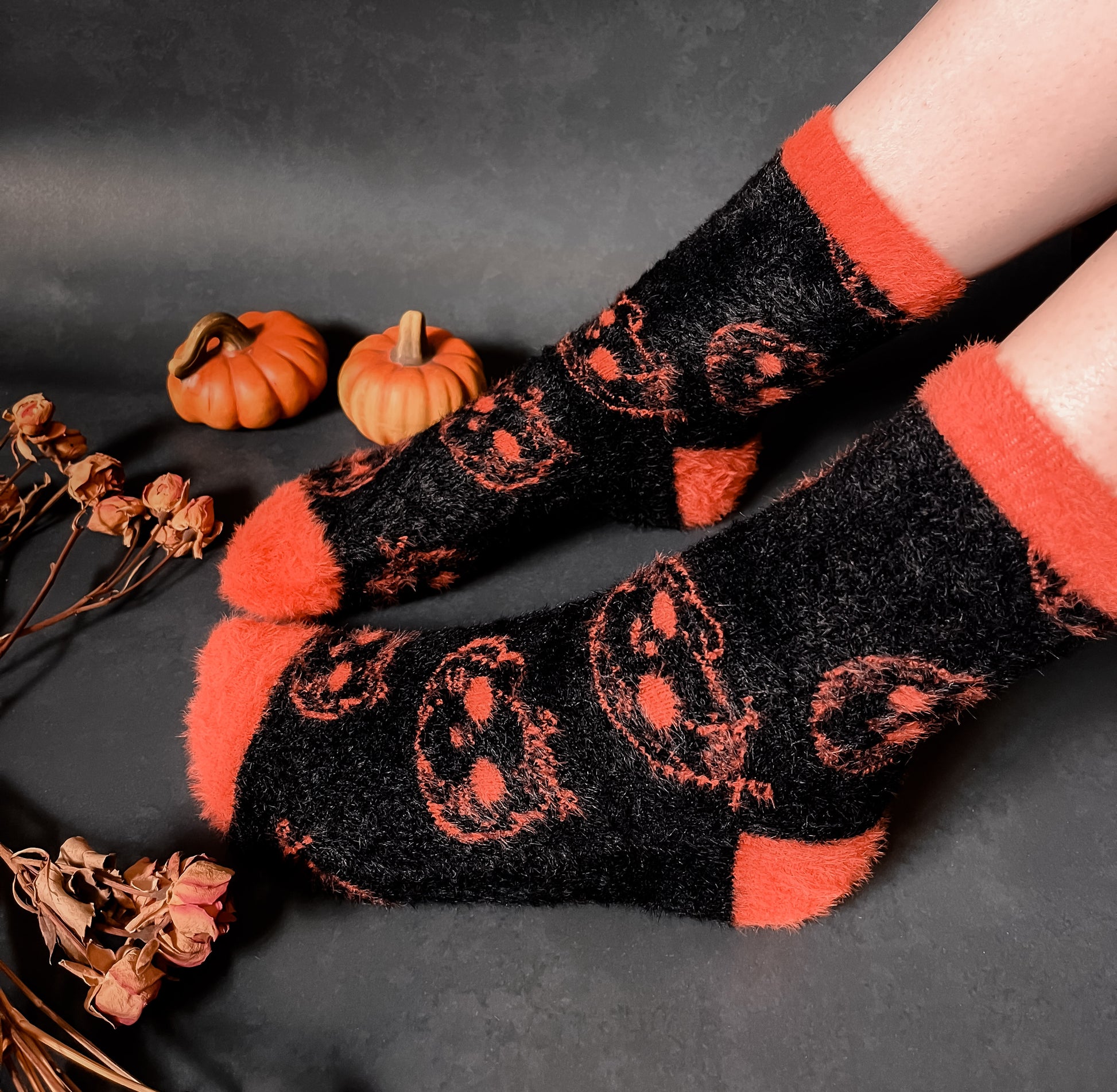 Black fuzzy socks with orange on the toe, heel, and ankle featuring a pattern of pumpkin shaped cat heads.