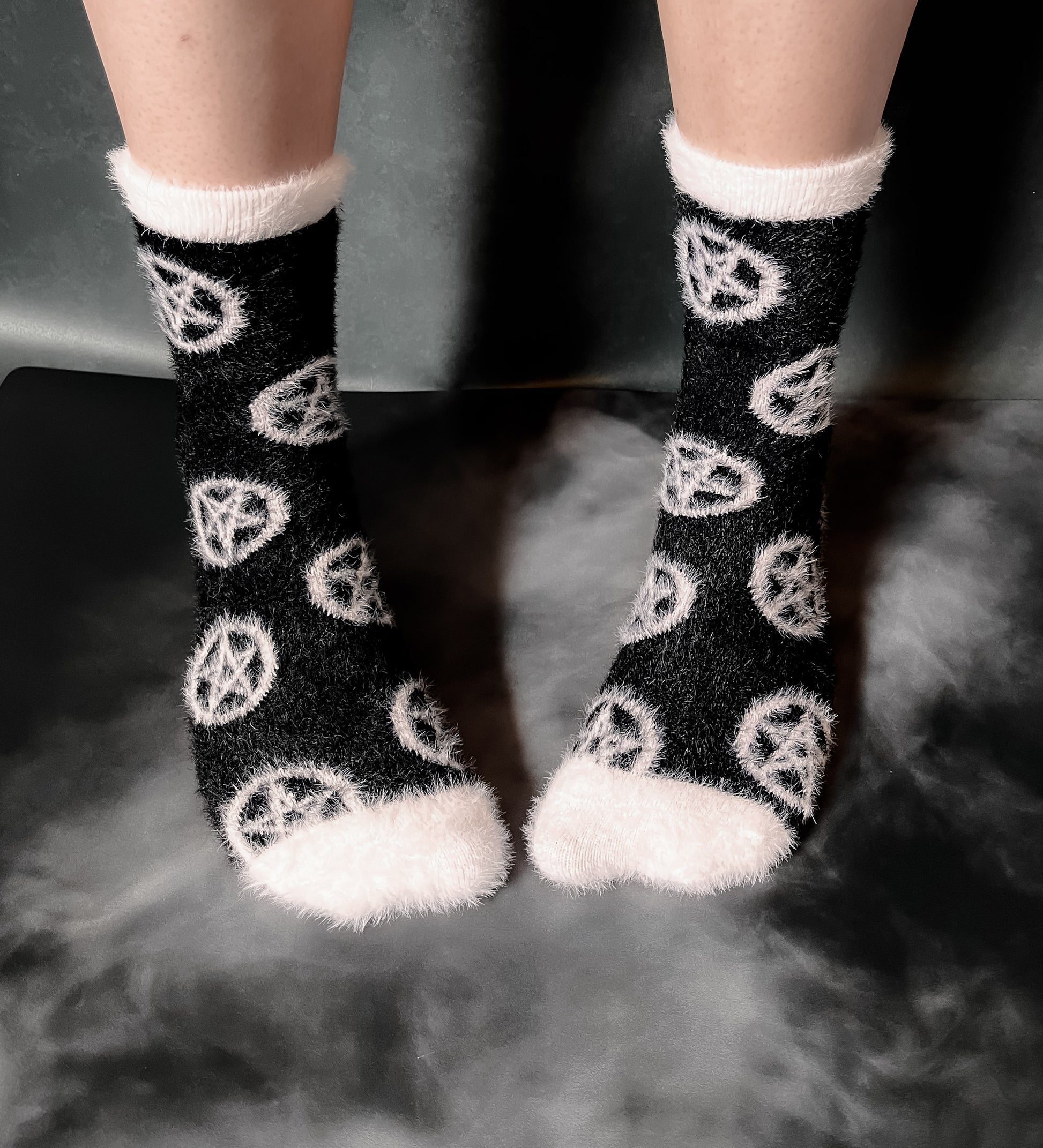 Black fuzzy socks with white on the toe, heel, and ankle featuring a pattern of pentagrams.