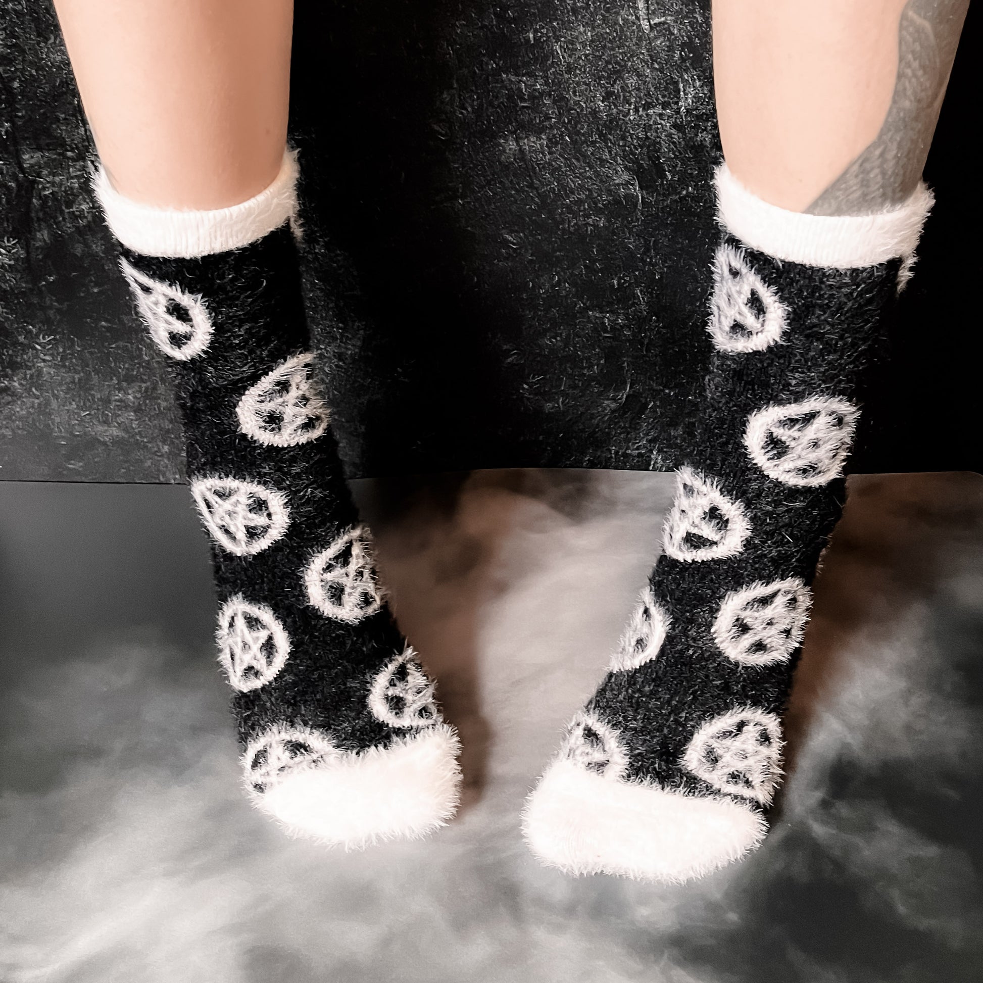 Black fuzzy socks with white on the toe, heel, and ankle featuring a pattern of pentagrams.
