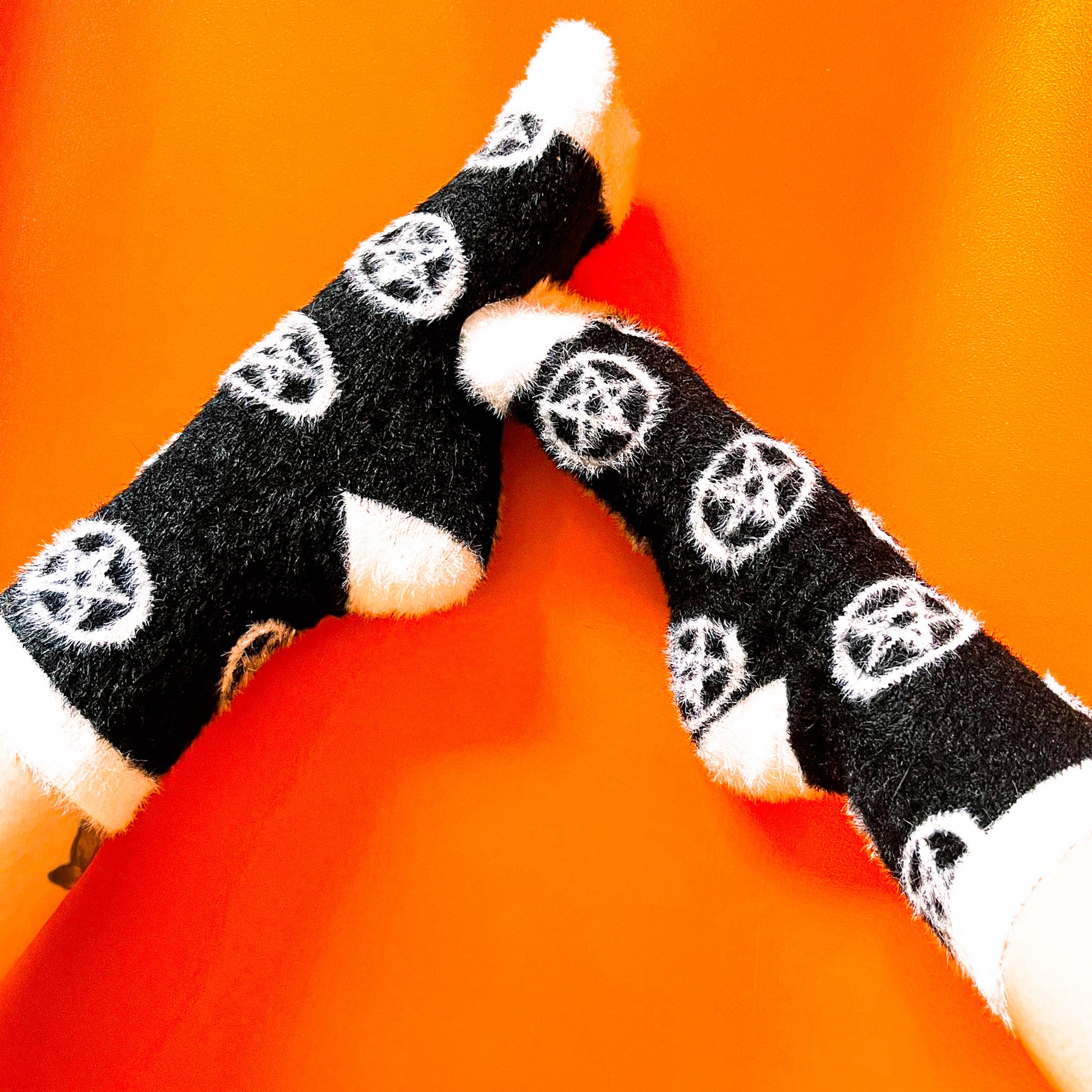Black fuzzy socks with white on the toe, heel, and ankle featuring a pattern of pentagrams.