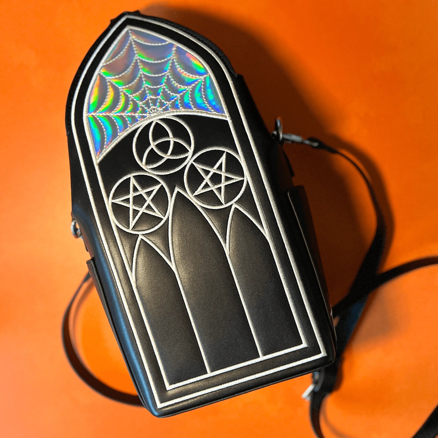 A black purse featuring Gothic inspired architecture. The top has a holographic spiderweb design.