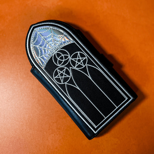 A black wallet featuring Gothic inspired architecture. The top has a holographic spiderweb design.