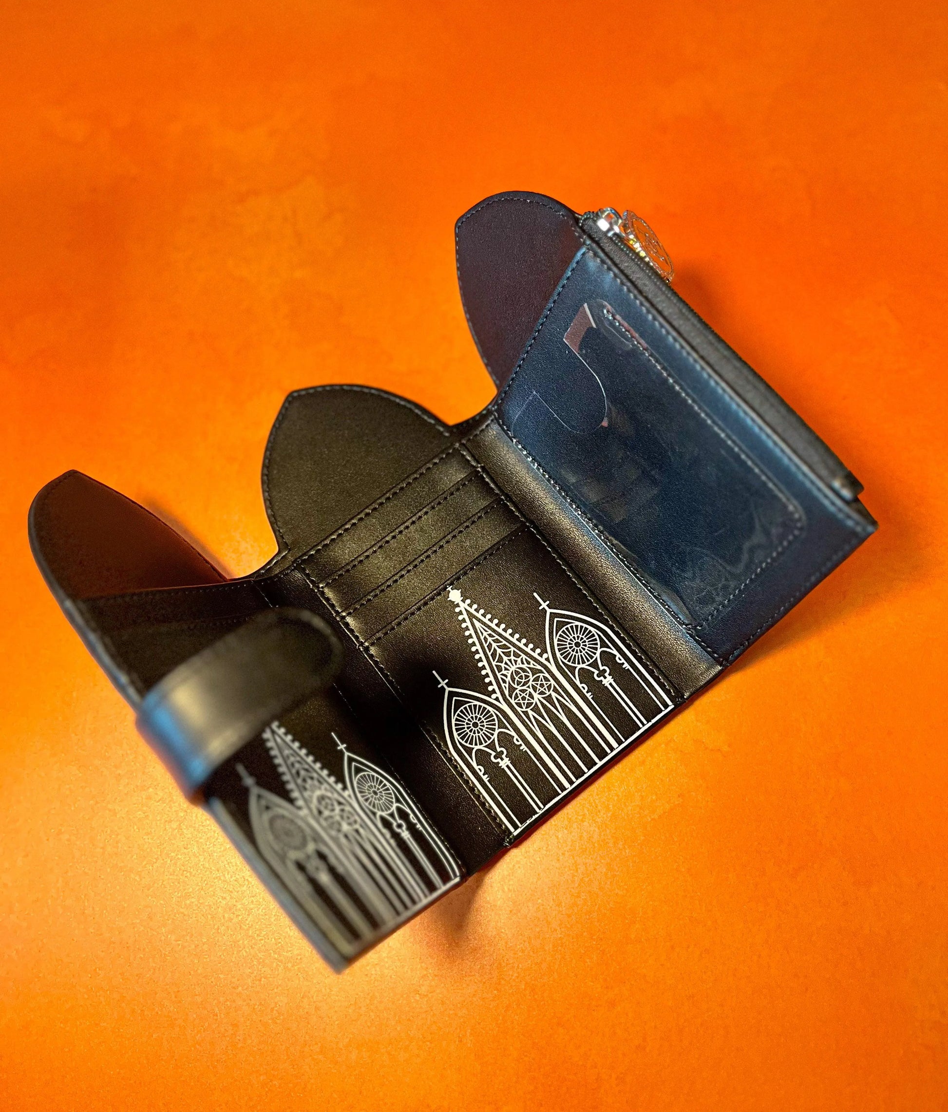 A black wallet opened up in a tri-fold style featuring Gothic inspired architecture.