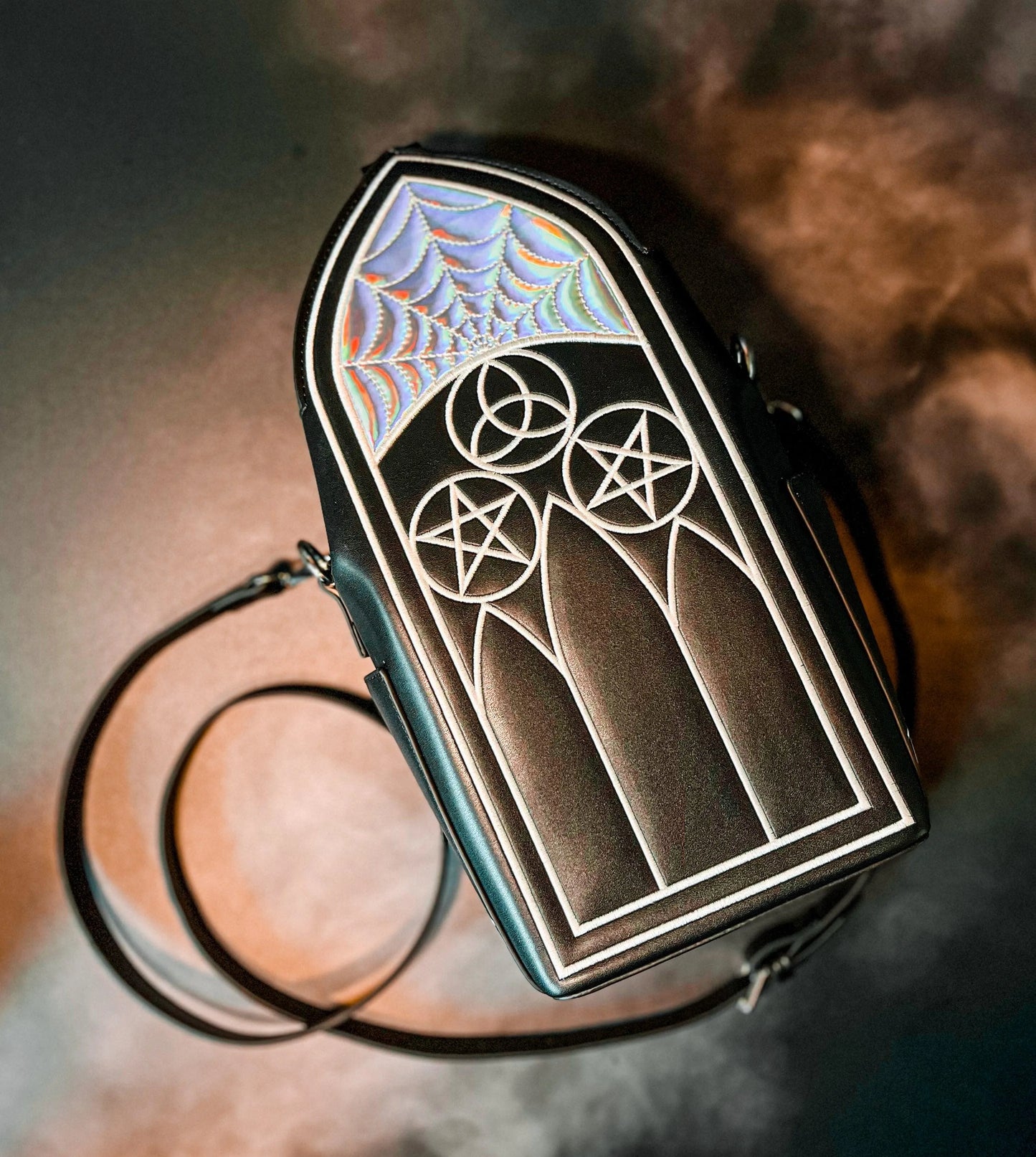 A black purse featuring Gothic inspired architecture. The top has a holographic spiderweb design.