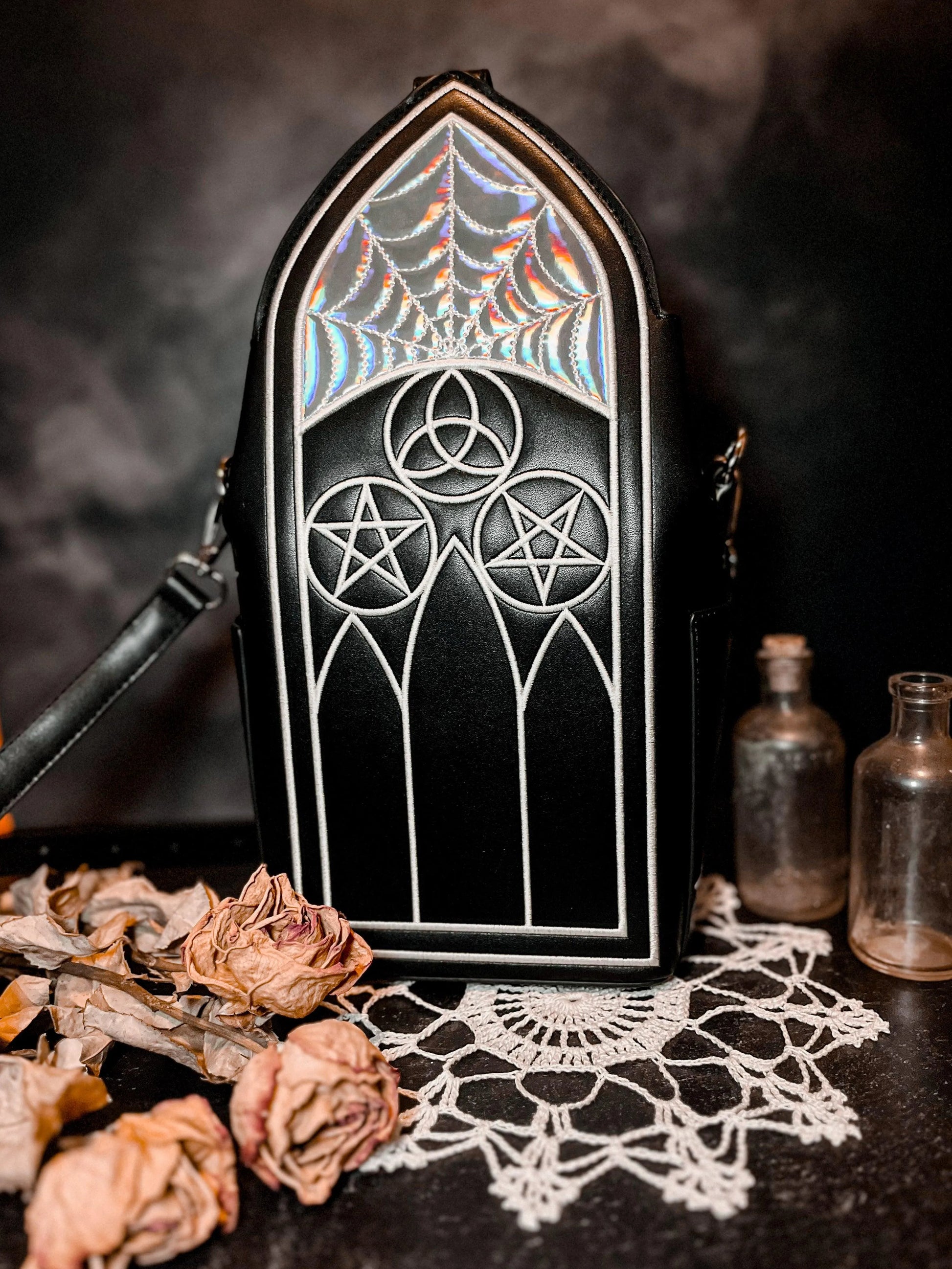 A black purse featuring Gothic inspired architecture. The top has a holographic spiderweb design.