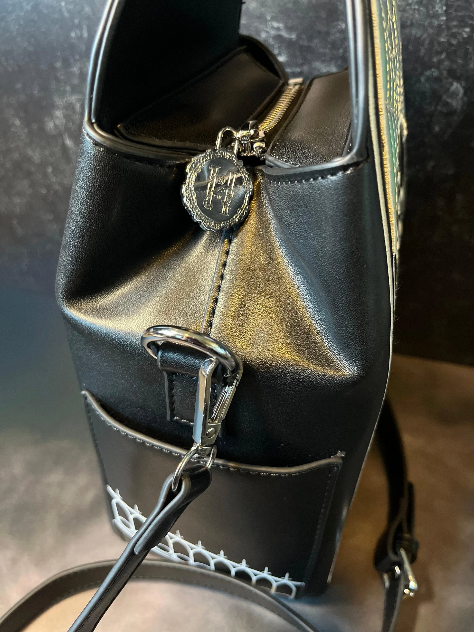 The side view of a gothic black bag featuring a keychain with the letter "H" on it.