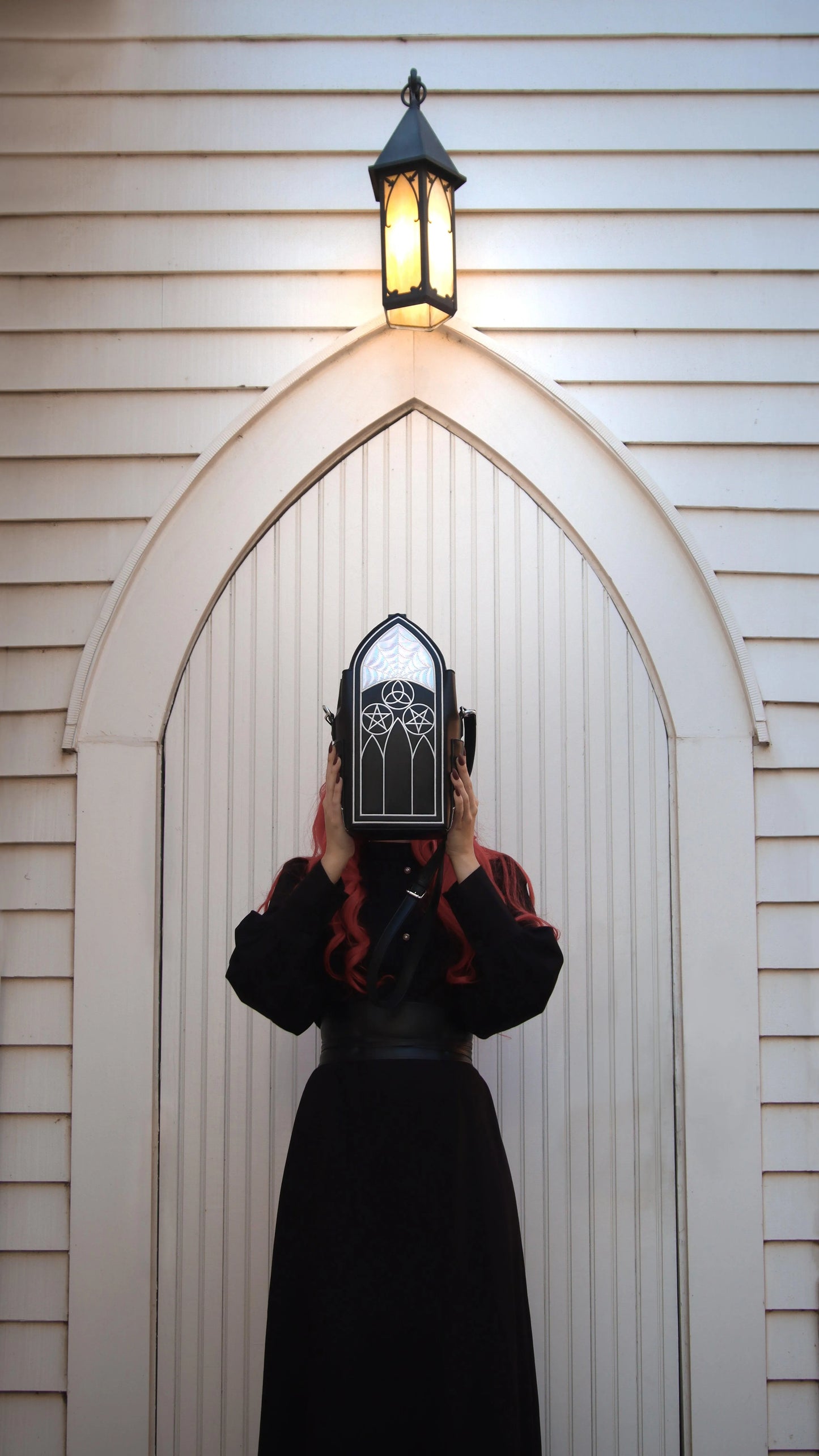 Women with long red hair and a long black dress with a gothic-styled bag held in front of her face.