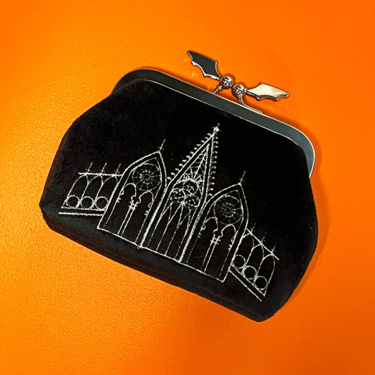 Black coin purse featuring gothic gables. The clasp of the purse in the shape of a bat. The bag is on top of an orange background.