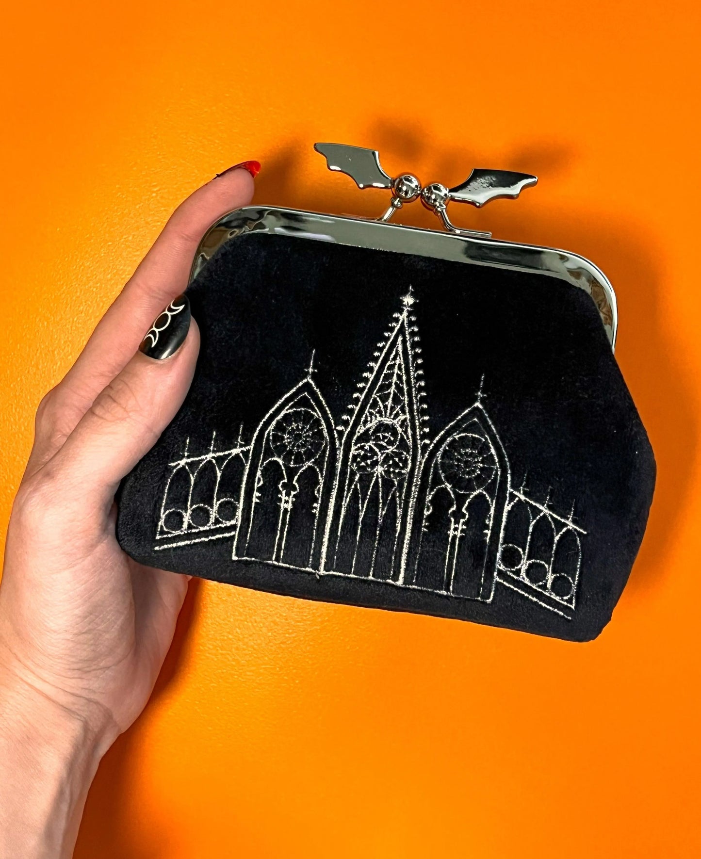Black coin purse featuring gothic gables. The clasp of the purse in the shape of a bat. The bag is on top of an orange background.