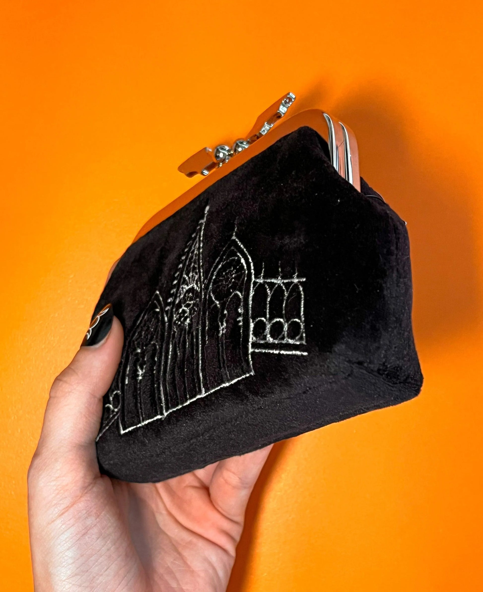 Black coin purse featuring gothic gables. The clasp of the purse in the shape of a bat. The bag is on top of an orange background.