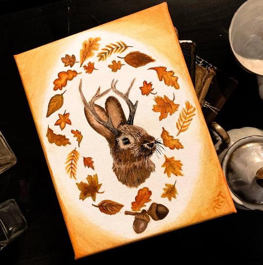 A print of a cryptid jackalope surrounded by orange leaves and  acorns.