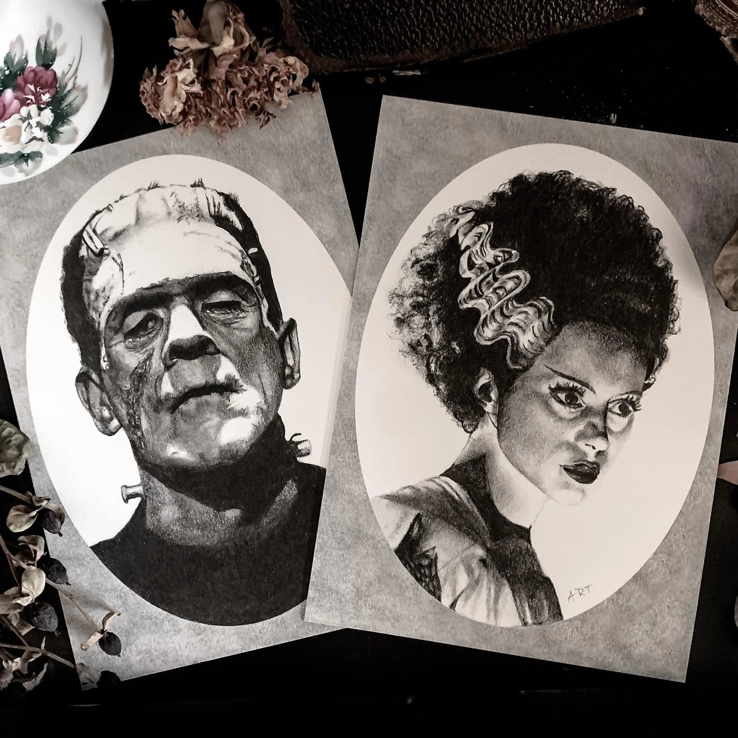 Black and white portrait drawing of Frankenstein's monster and the Bride of Frankenstein on a white oval surrounded by a grey rectangle.