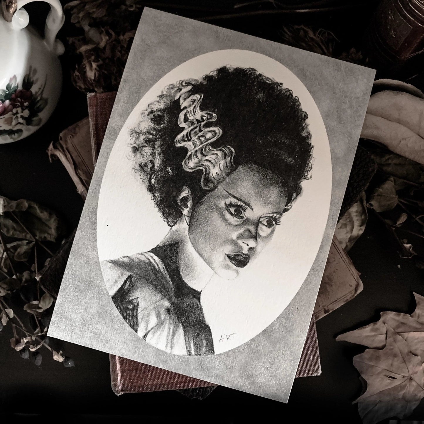 Black and white portrait drawing of the Bride of Frankenstein on a white oval surrounded by a grey rectangle.