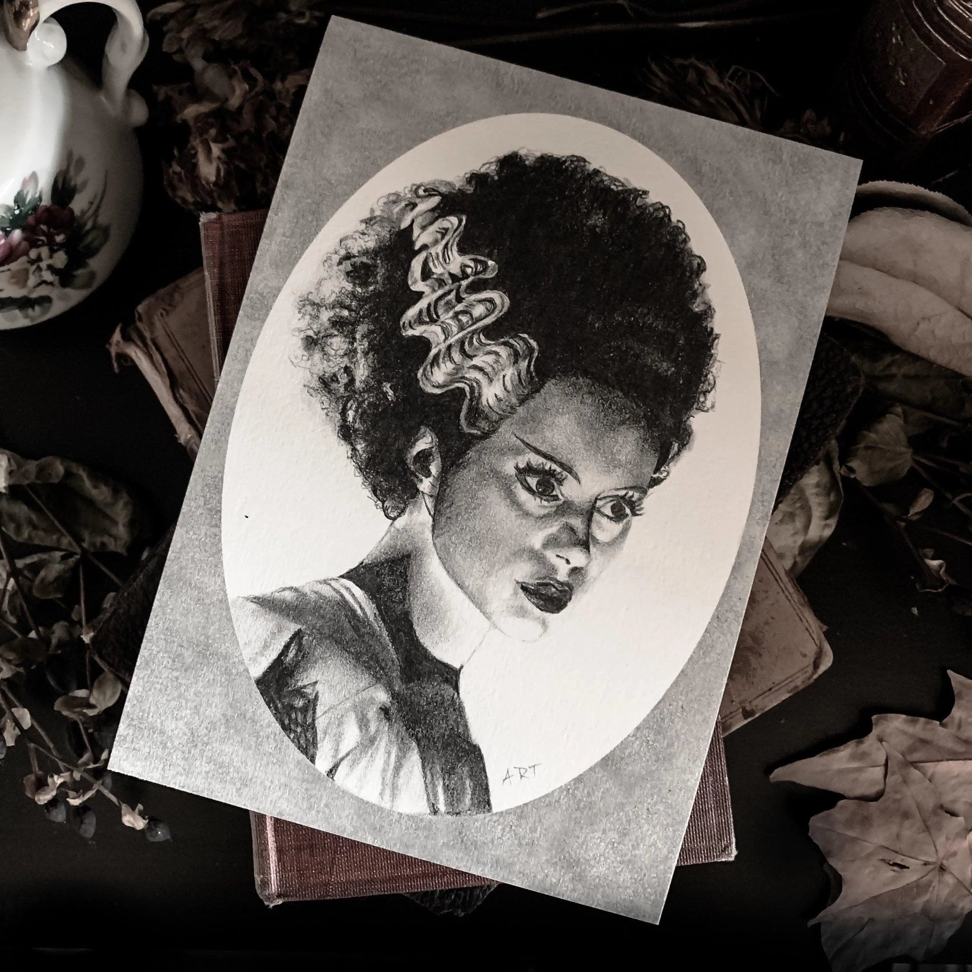 Black and white portrait drawing of the Bride of Frankenstein on a white oval surrounded by a grey rectangle.