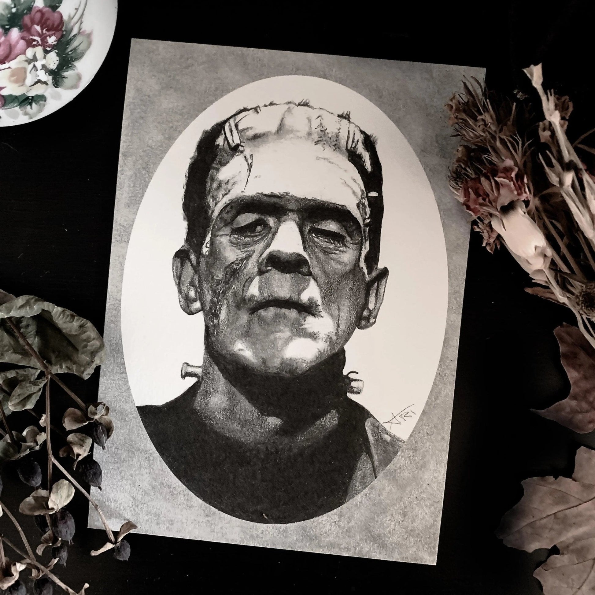 Black and white portrait drawing of Frankenstein's monster on a white oval surrounded by a grey rectangle.