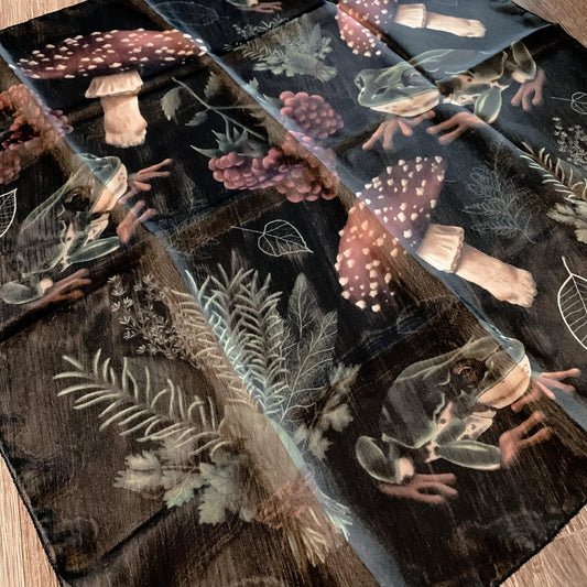 Cloth/scarf featuring a pattern of mushrooms, plants, and frogs on a black background.