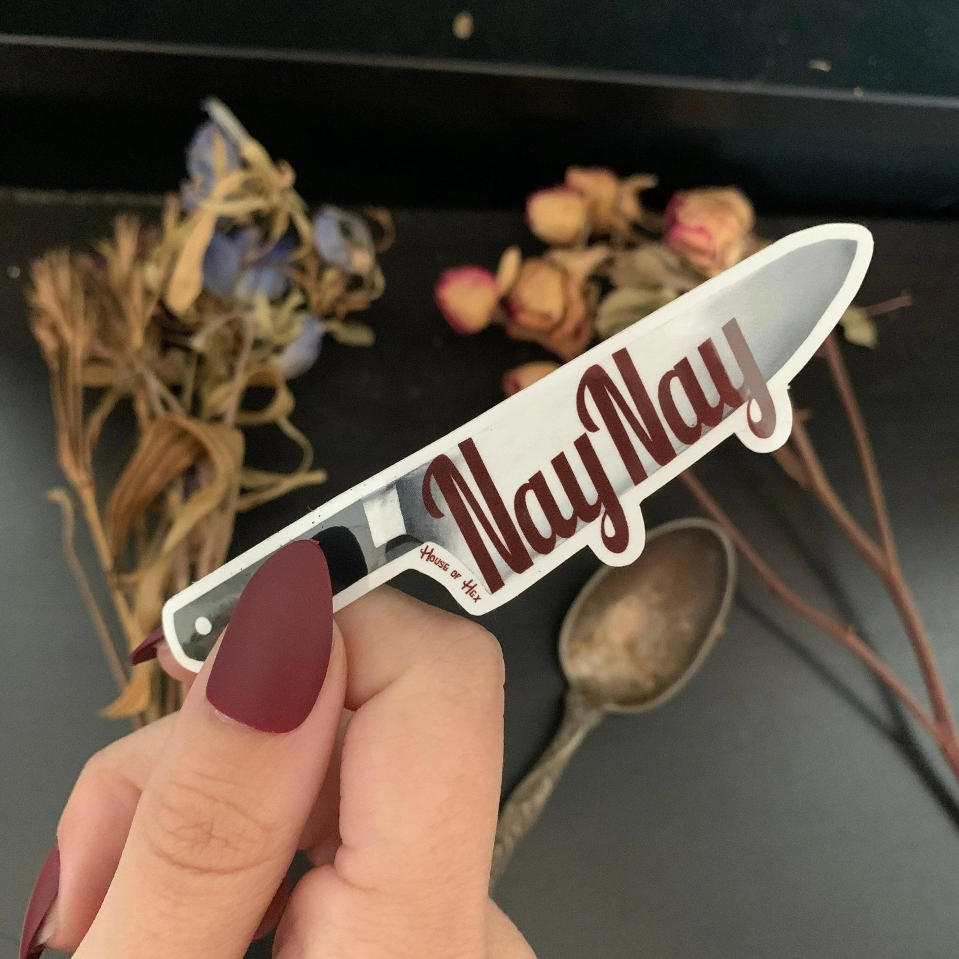 A sticker of a knife displaying the word "NayNay" in maroon on the blade with a white border around the knife.