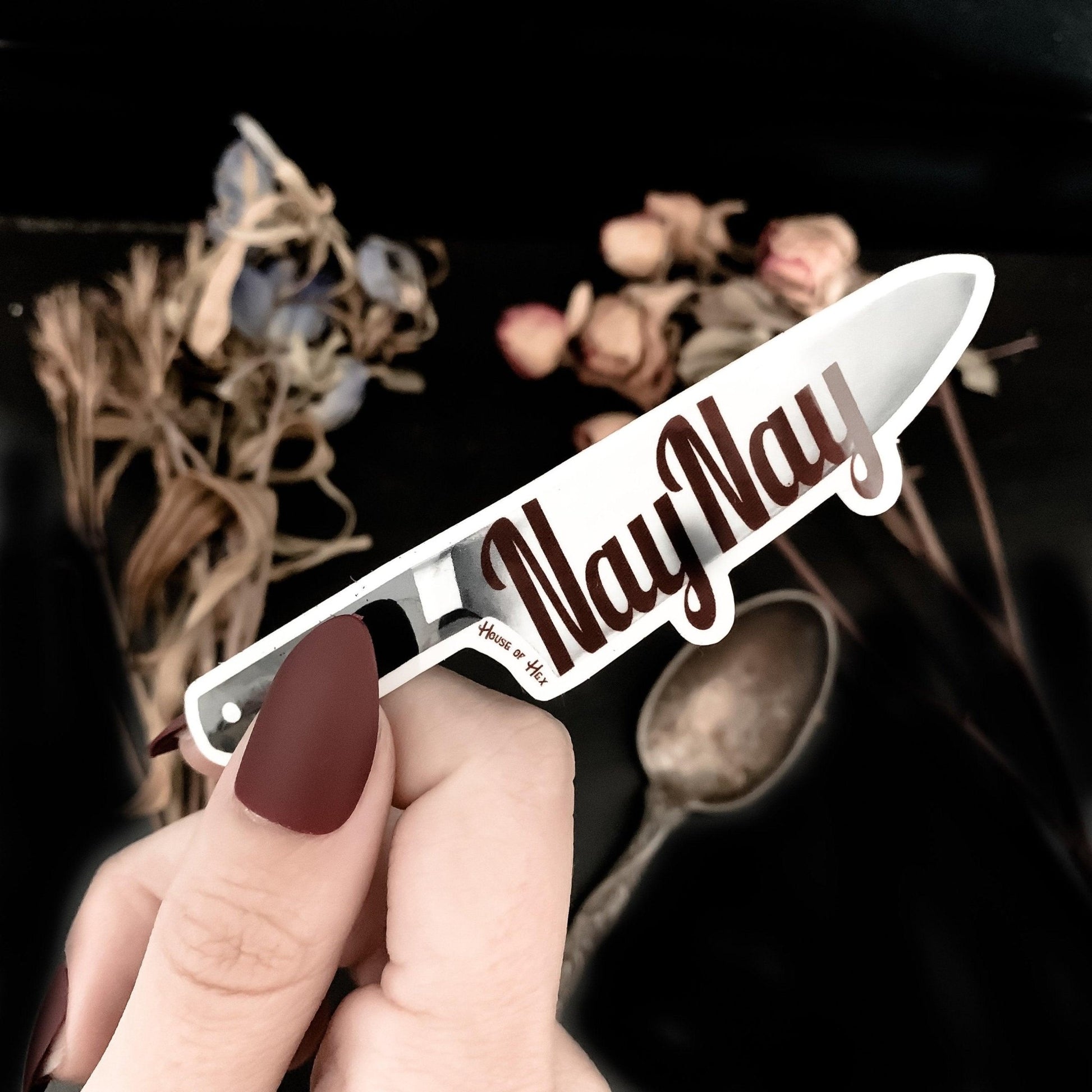 A sticker of a knife displaying the word "NayNay" in maroon on the blade with a white border around the knife.
