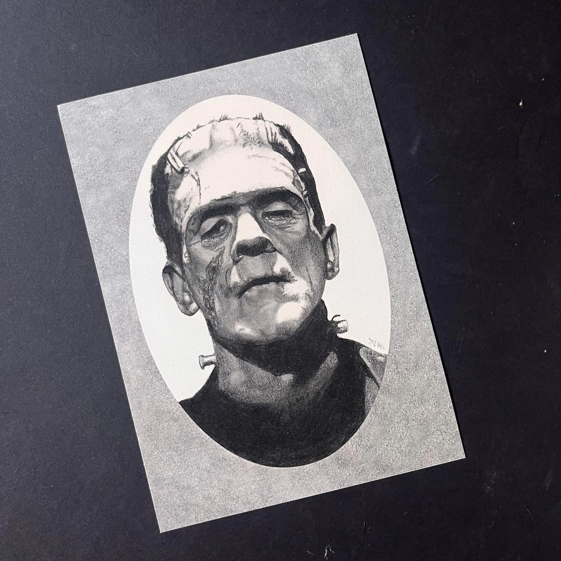 Black and white portrait drawing of Frankenstein's monster on a white oval surrounded by a grey rectangle.
