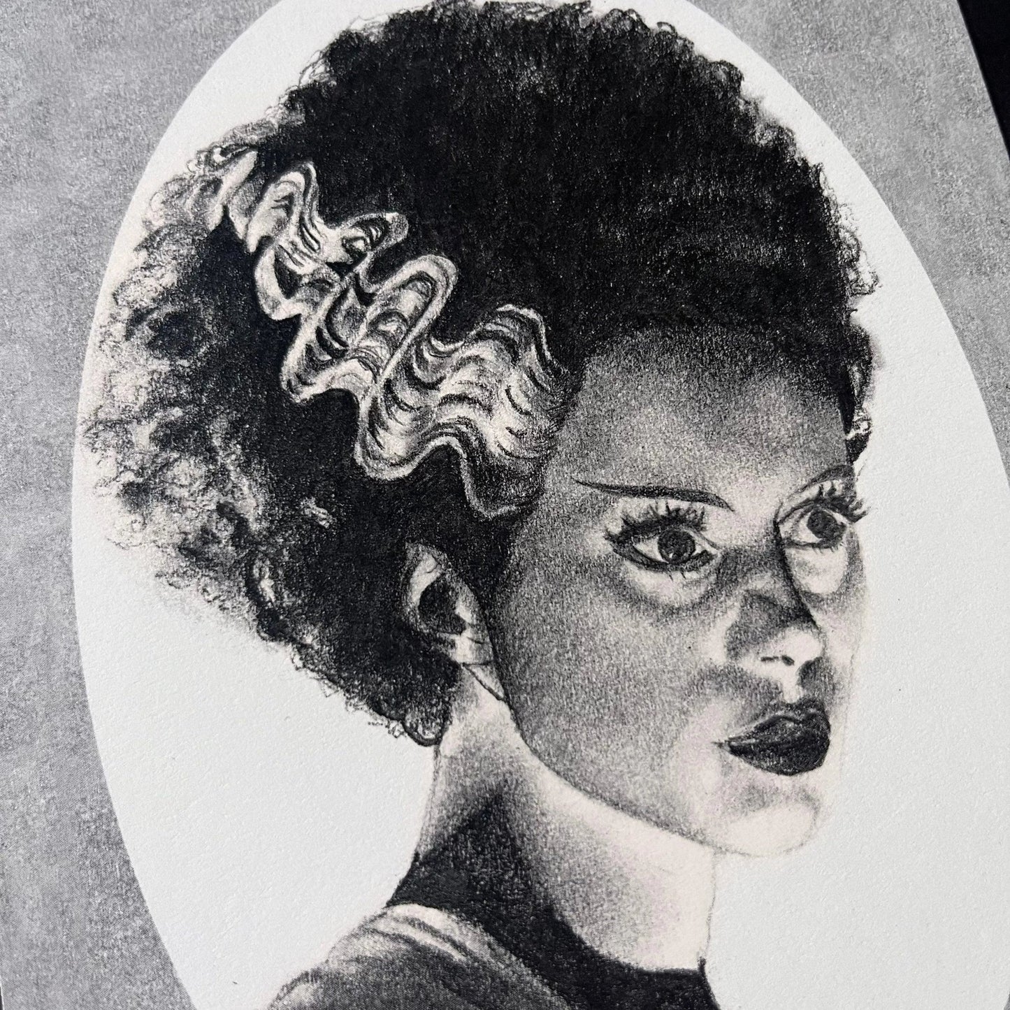 Black and white portrait drawing of the Bride of Frankenstein on a white oval surrounded by a grey rectangle.