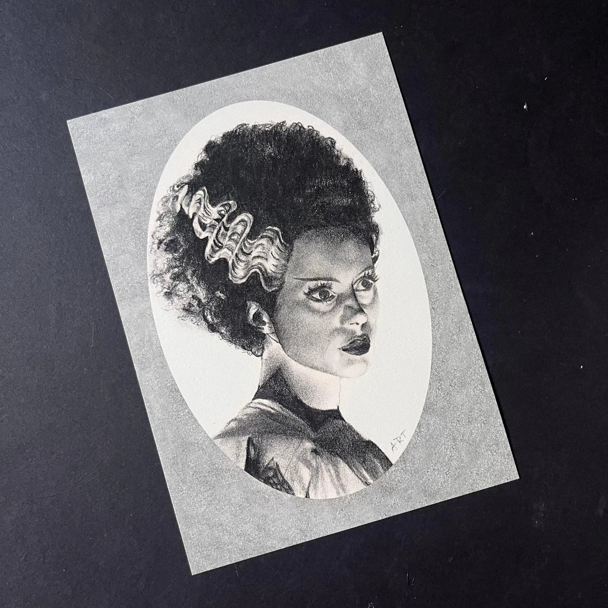 Black and white portrait drawing of the Bride of Frankenstein on a white oval surrounded by a grey rectangle.