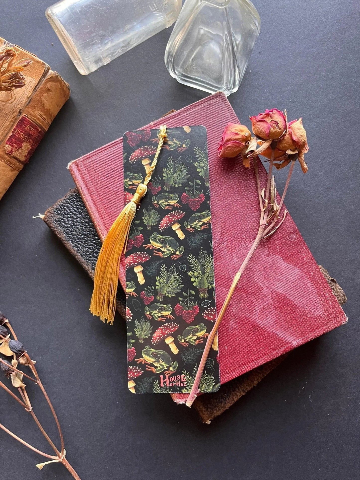 A decorative bookmark featuring a pattern of mushrooms, plants, and frogs on a black background with a gold tassel.