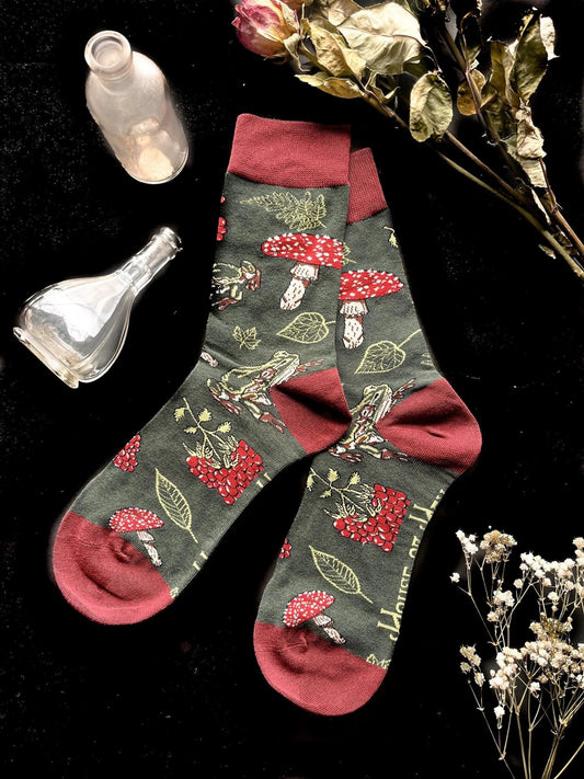 Socks with red on the toes, heel, and ankle section featuring a pattern of mushrooms, plants, and frogs on a green background.