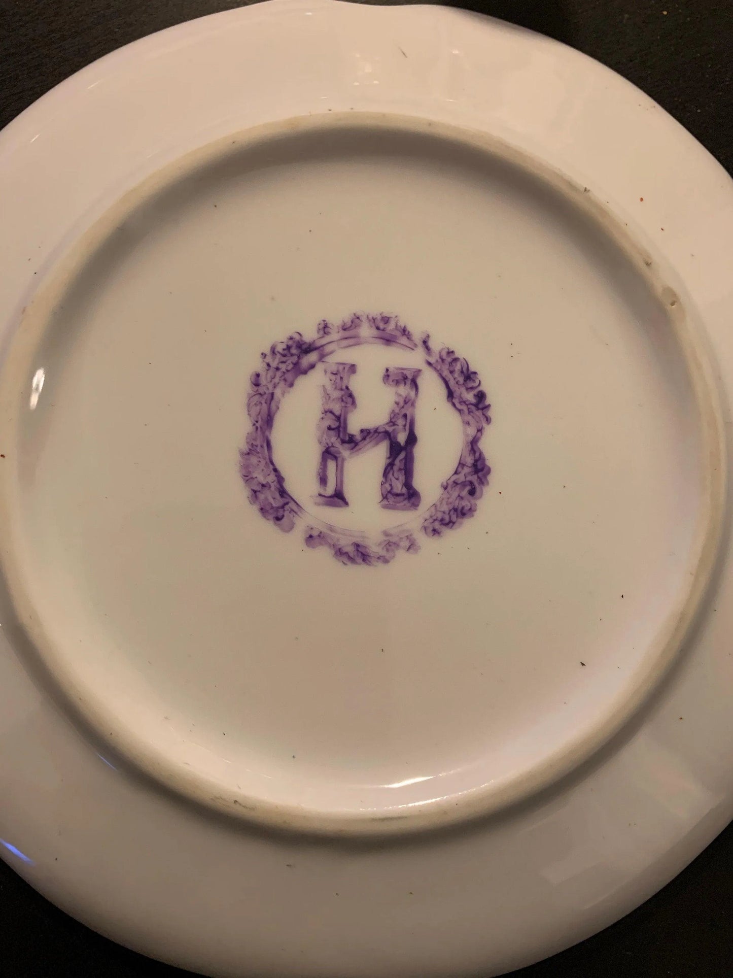 The bottom of a white decorative plate with an "H" in the center.