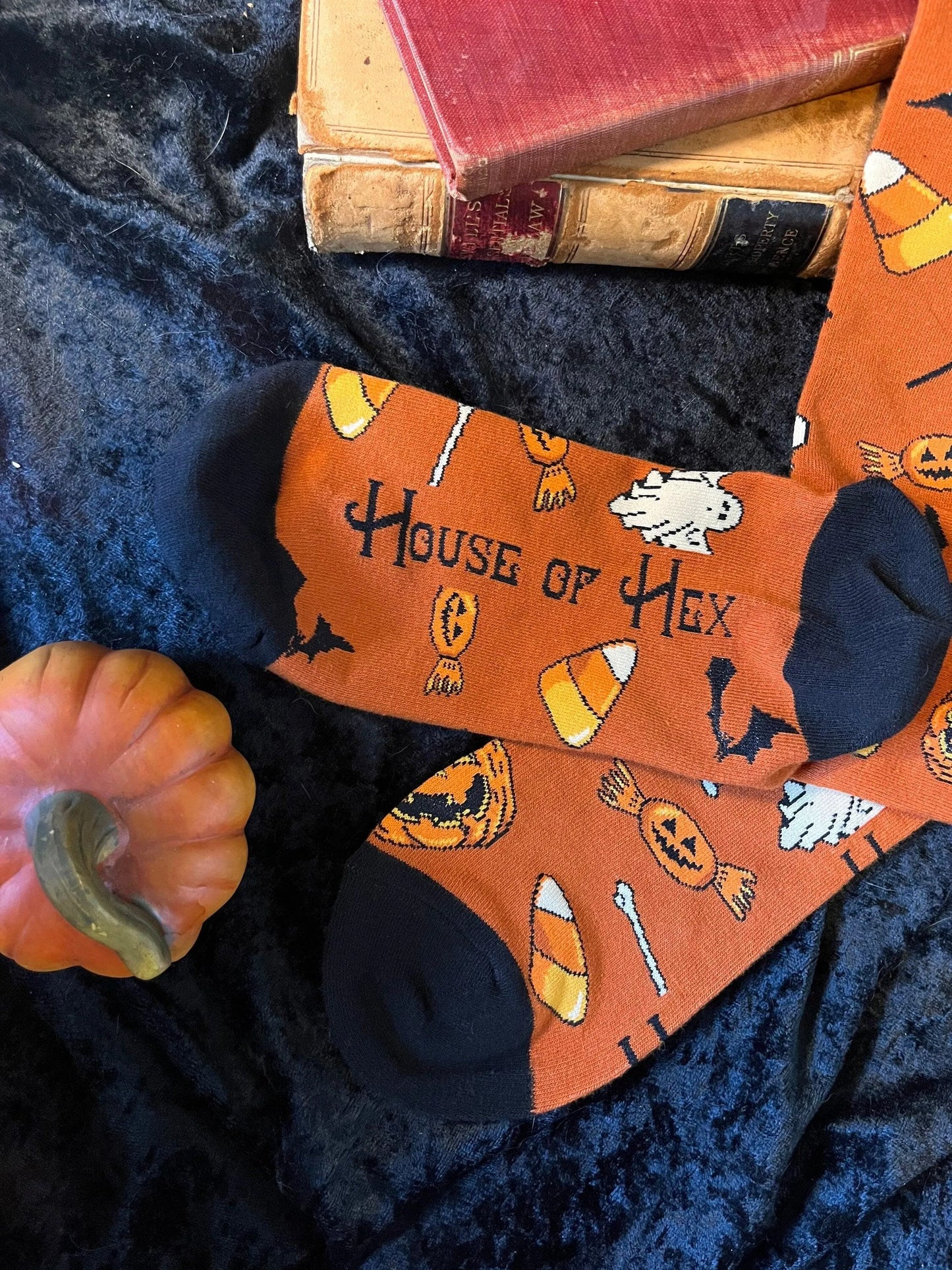 Halloween socks with blacks on the toes, heel, and ankle section featuring a pattern of pumpkins, candy corn, ghosts, bones, and bats. On the bottom is says "House of Hex".