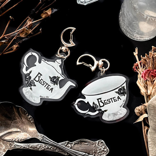 Two elegant white tea cups with the word "Bestea" written in a gothic font with a golden moon clasp keychain on the top.