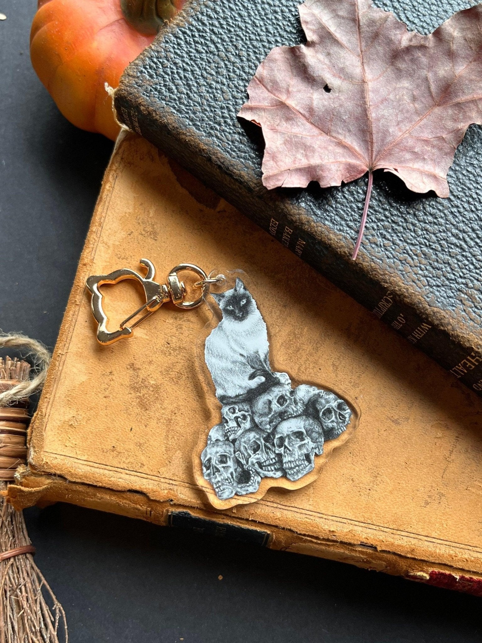 A black and white keychain with a drawing of a cat perched atop a collection of skulls with a golden cat-shaped clasp.