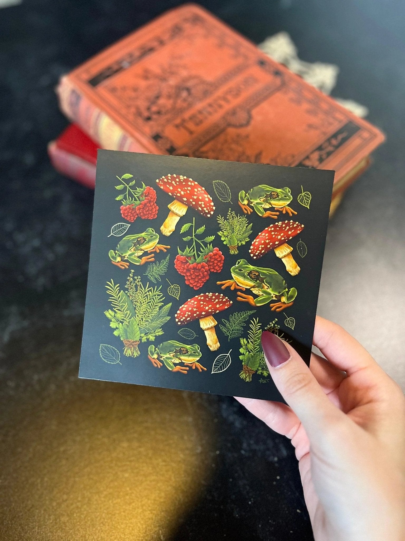 A decorative square print featuring a pattern of mushrooms, plants, and frogs on a black background.