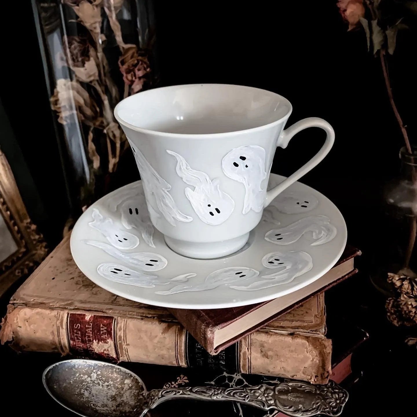 A decorative white cup and saucer featuring a pattern of ghosts.