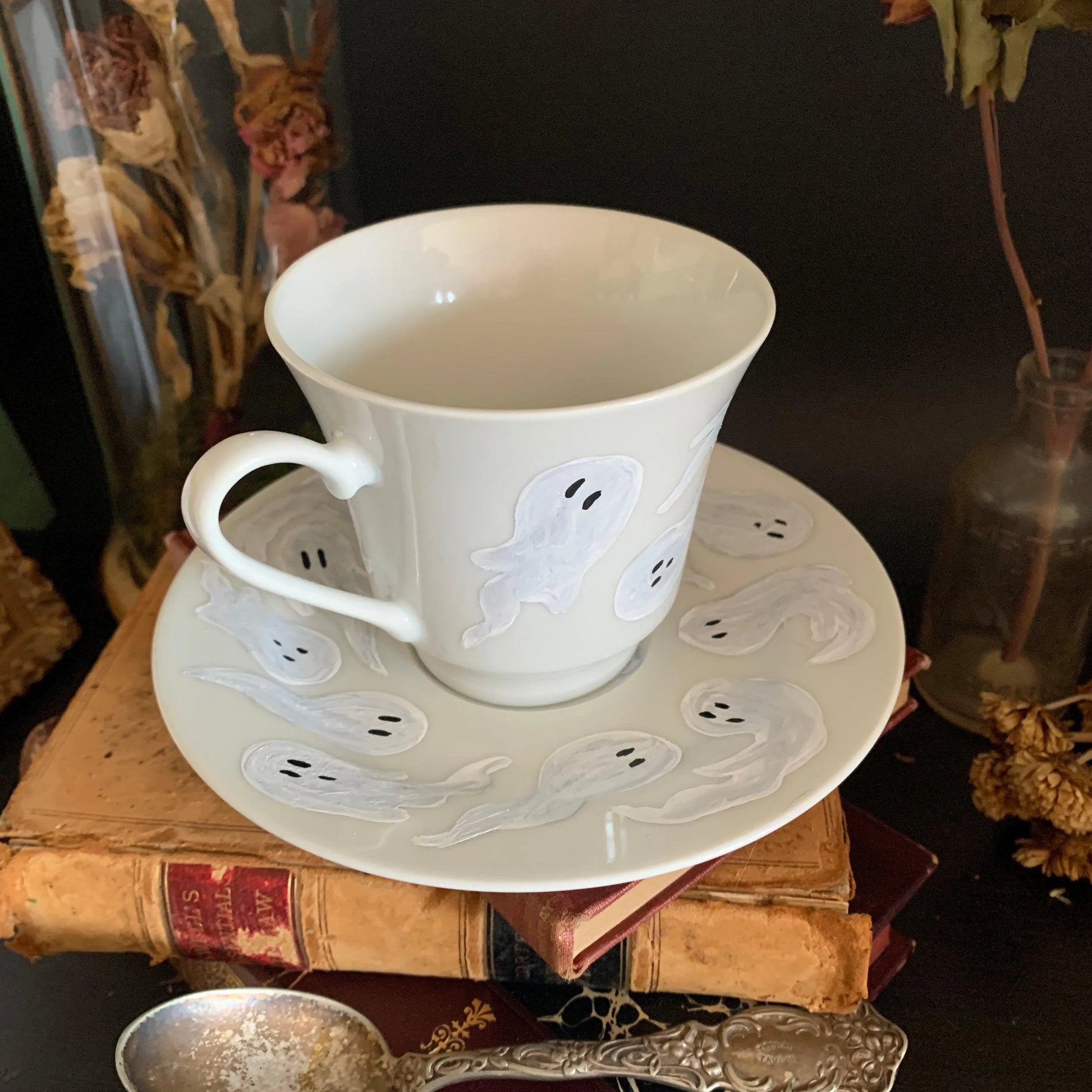 A decorative white cup and saucer featuring a pattern of ghosts.