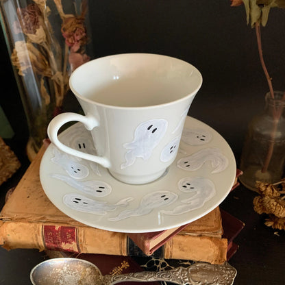 A decorative white cup and saucer featuring a pattern of ghosts.